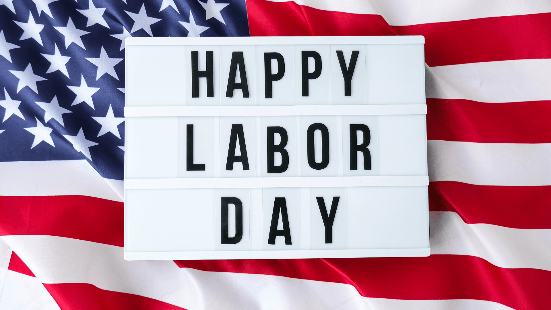 A sign that says Happy Labor Day on top of the U.S. flag.
