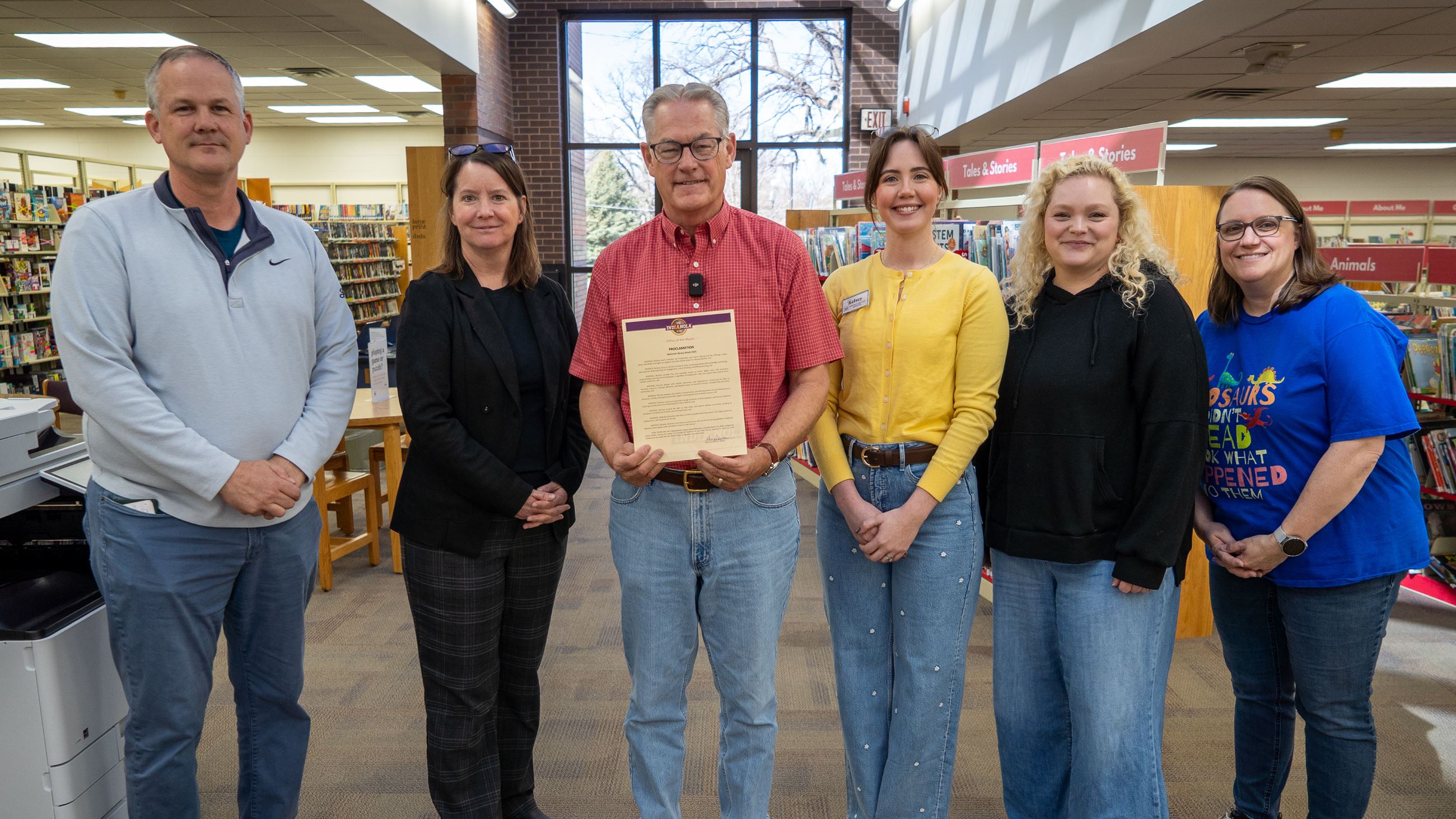 A group of people standing inside a library hallway smiling after a proclamation is read aloud.