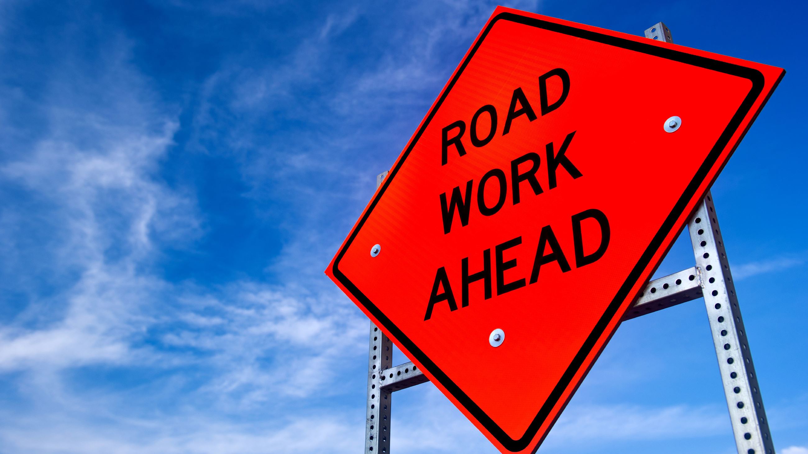 An orange sign that indicates road work ahead on a street.
