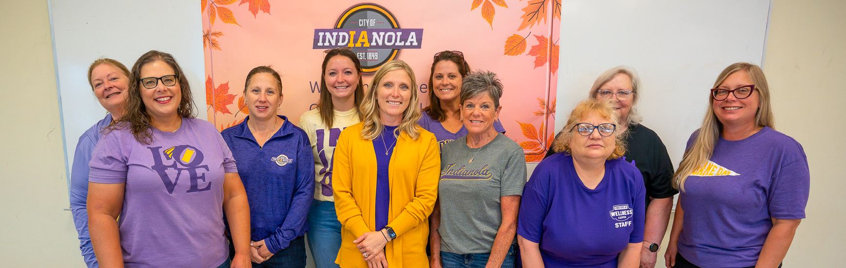 A group of City of Indianola employees smile and pose for a photo wearing Indianola School colors.