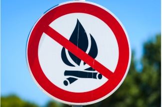 A circular sign with a red prohibition symbol overlays a burning log, indicating no open burning.