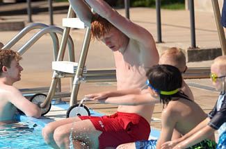 A group of children learn swim lessons from a lifeguard at the pool.