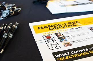 A Hands-Free Driving Law informational sheet sits on a table next to Indianola Police pens.