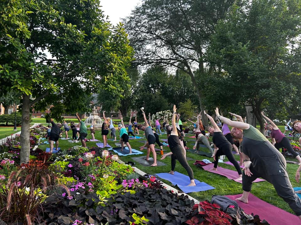 People doing yoga poses in a park with flowers and a fountain
